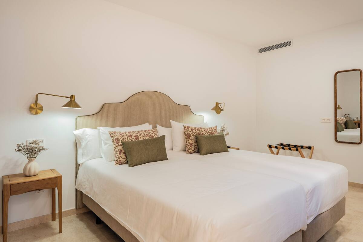 A neatly made bed with white bedding, a wooden headboard, and two bedside lamps.