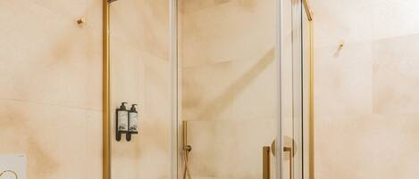 A modern bathroom with a glass-enclosed shower, a toilet, and a sink with a towel rack.