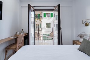 Habitación de hotel con cama, escritorio, silla y balcón con mesa y sillas.
