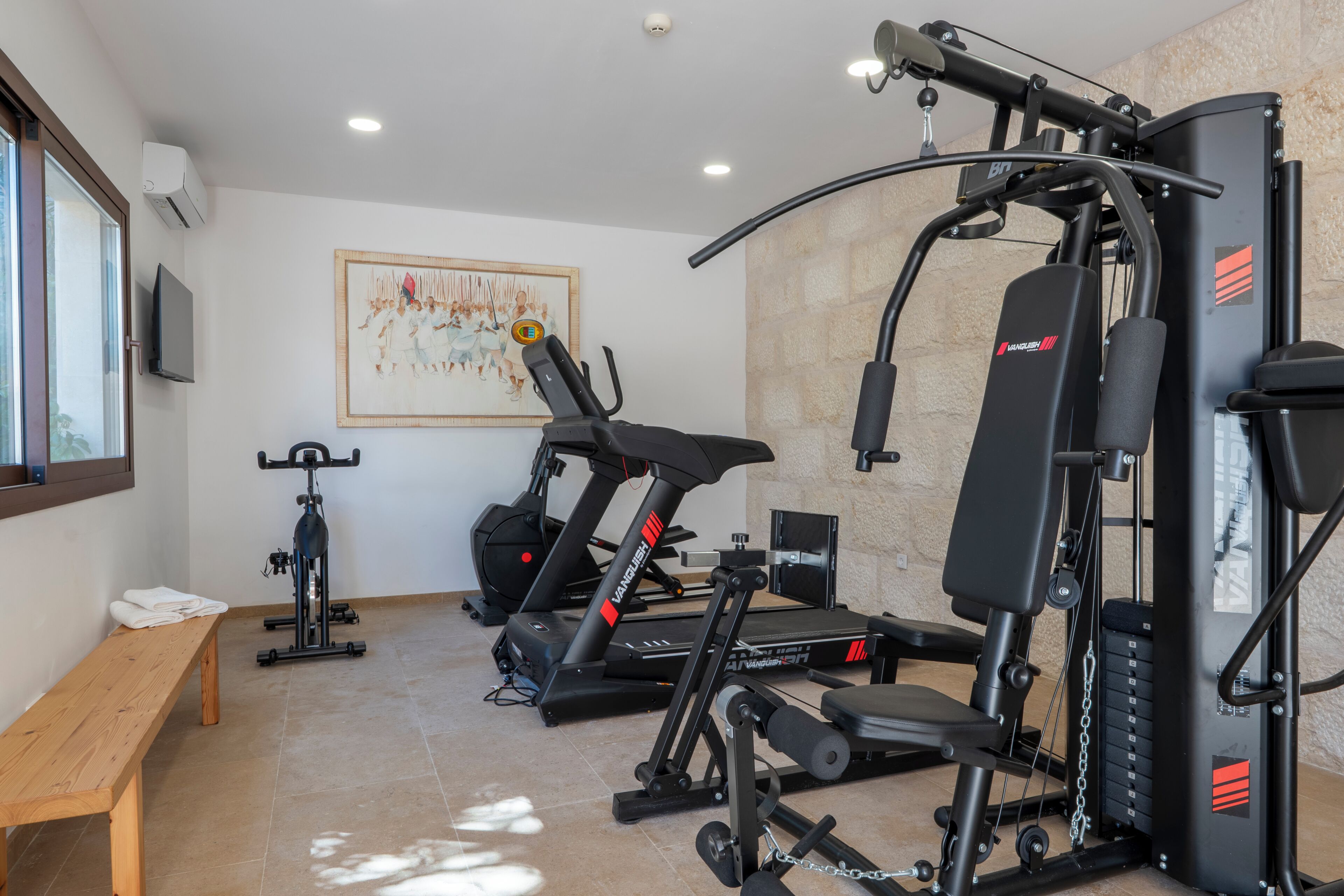 A gym with exercise equipment, a bench, and a wall-mounted TV.