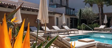 A poolside area with lounge chairs and umbrellas, a clear blue sky, and a building with a white facade.