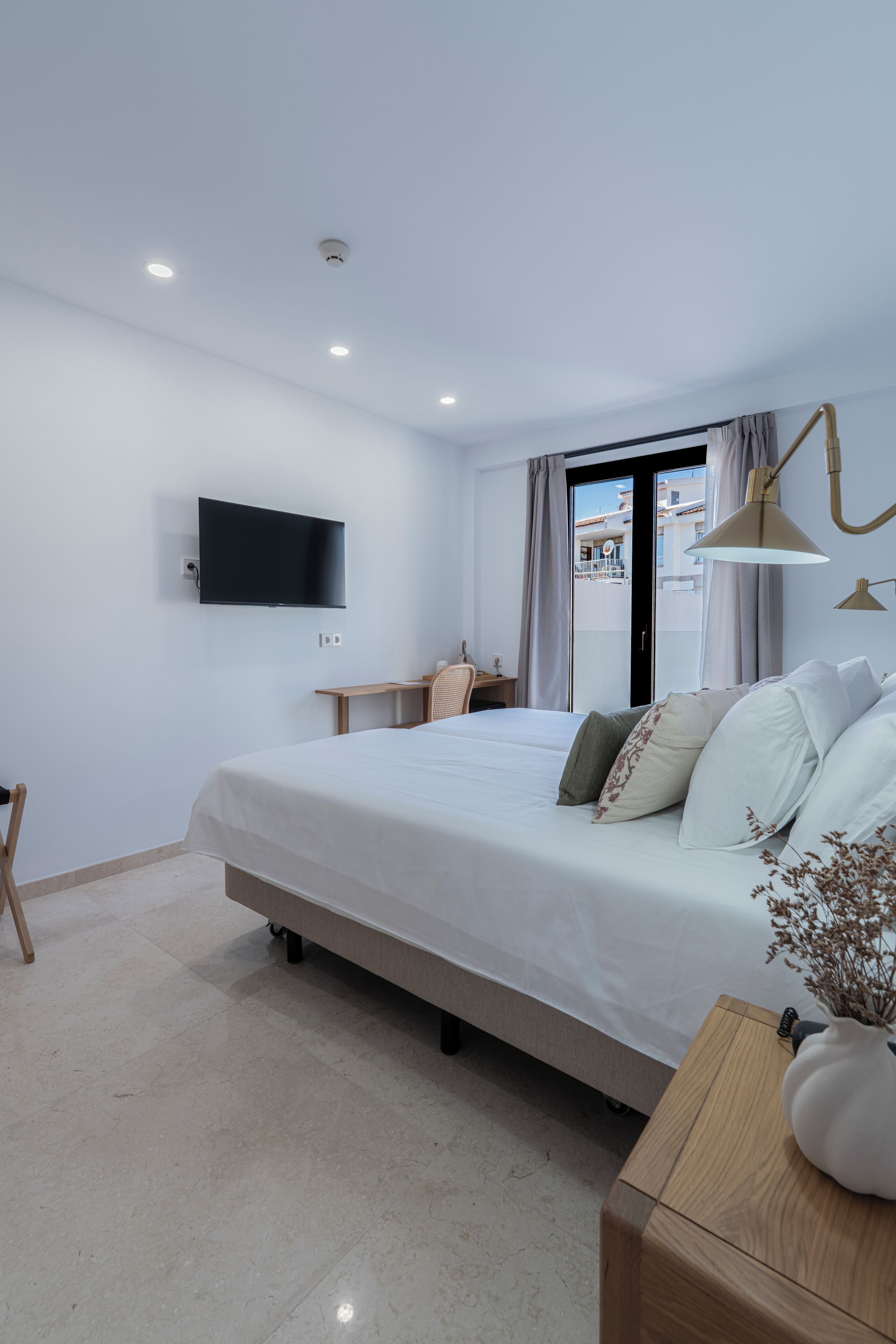 Una habitació d'hotel moderna amb un llit, una taula de treball, una televisió i una finestra amb cortines.
