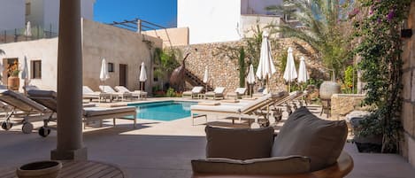 Zona junto a la piscina con sillones de descanso, sombrillas y un muro de piedra.