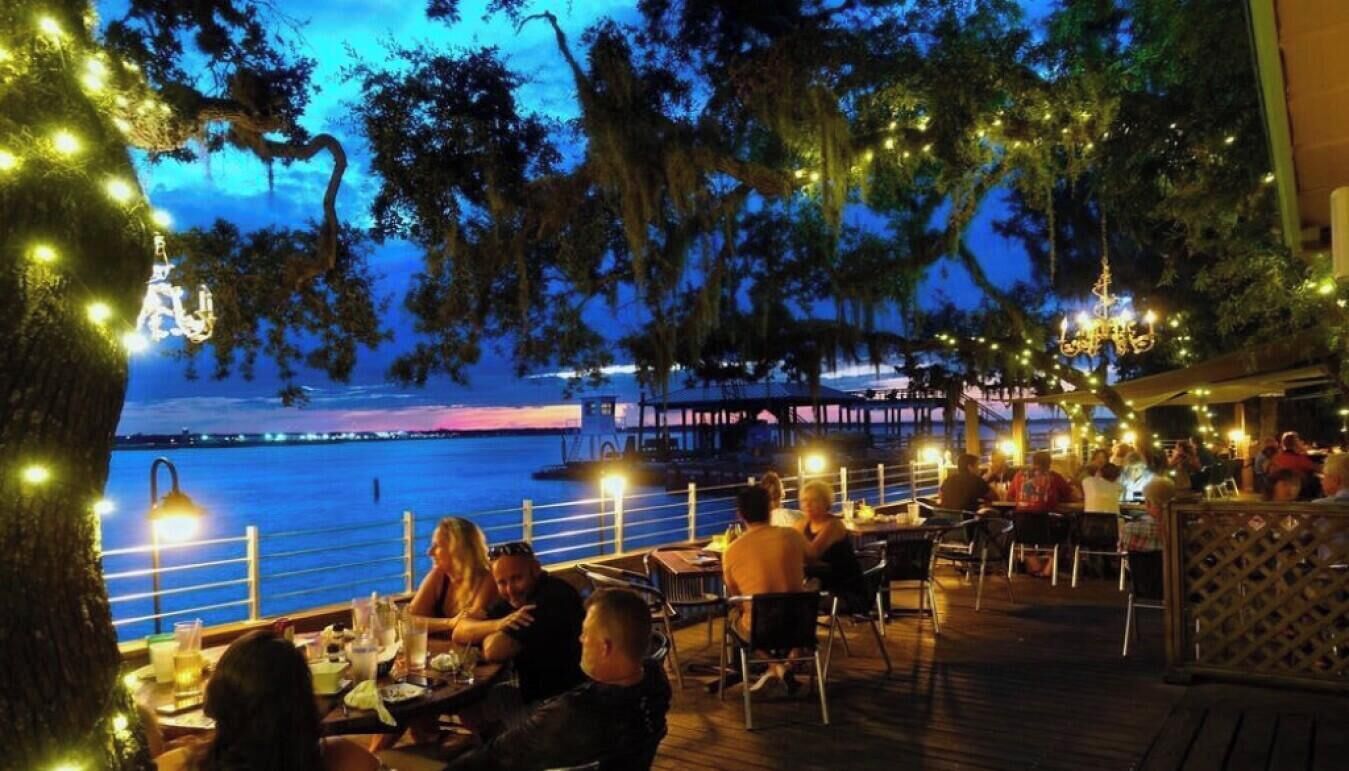 Un espace de restauration en plein air, avec des tables et des chaises, offrant une vue sur un plan d’eau et un quai.