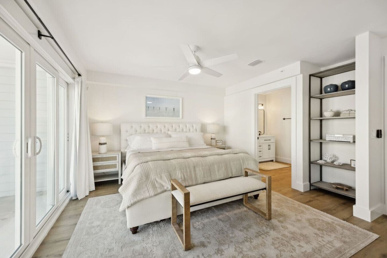 Une chambre à coucher comprenant un lit, des tables de chevet, un banc, un ventilateur de plafond et une armoire.