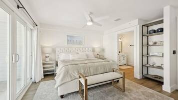 Une chambre à coucher comprenant un lit, des tables de chevet, un banc, un ventilateur de plafond et une armoire.