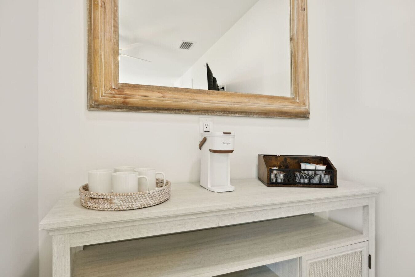A white console table with a coffee maker, a basket of white mugs, and a box of tissues.