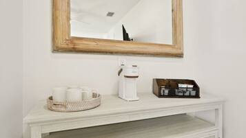 A white console table with a coffee maker, a basket of white mugs, and a box of tissues.