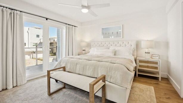 Une chambre à coucher comprenant un lit, un banc, une table de chevet, un ventilateur de plafond et une vue sur l’extérieur, accessible par une porte coulissante.