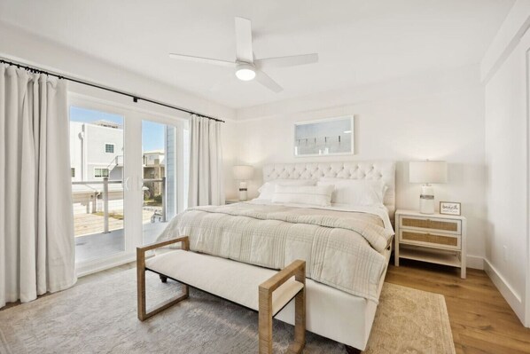 A bedroom with a bed, a bench, a nightstand, a ceiling fan, and a view through a sliding door.