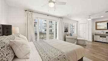 A bedroom with a bed, a nightstand, a chair, a dresser, a ceiling fan, and a large window with curtains.