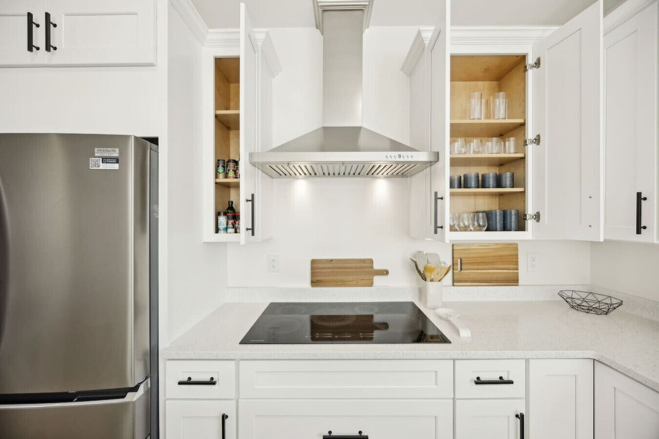 A modern kitchen with white cabinetry, a stainless steel refrigerator, a built-in stove, and wooden shelves.