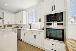 A modern kitchen with white cabinetry, a stainless steel oven, and a large window. - NewConstructionLuxury|Pool|4beds|Downtown (St. Augustine)