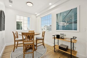 A dining area with a round table and four chairs, a bar cart with glasses, and a large window with a view of buildings. - NewConstructionLuxury|Pool|4beds|Downtown (St. Augustine)