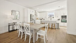 Une cuisine moderne avec des meubles blancs, un îlot central et un coin repas avec des chaises blanches.