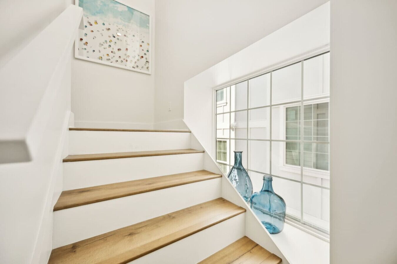 A staircase with wooden steps leading to a landing, a window with a grid pattern, and two blue glass bottles on the windowsill.