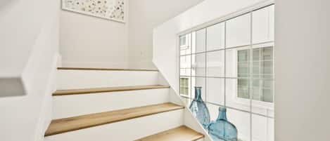 A staircase with wooden steps leading to a landing, a window with a grid pattern, and two blue glass bottles on the windowsill.