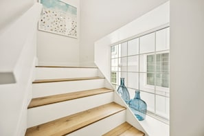 A staircase with wooden steps leading to a landing, a window with a grid pattern, and two blue glass bottles on the windowsill. - NewConstructionLuxury|Pool|4beds|Downtown (St. Augustine)