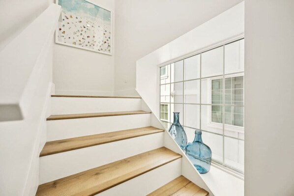 A staircase with wooden steps leading to a landing, a window with a grid pattern, and two blue glass bottles on the windowsill.