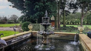 A multi-tiered fountain in a garden with a wooden deck and a pond.