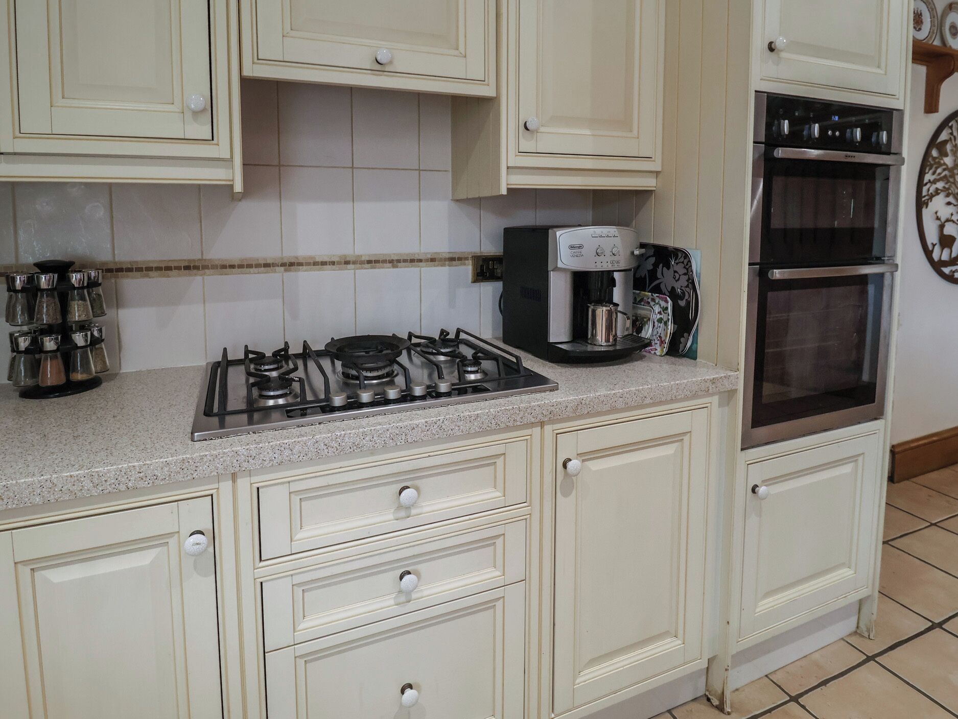 Una cocina con armarios blancos, estufa a gas, cafetera y horno doble.