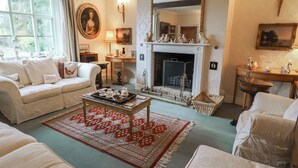 A traditional living room with a fireplace, white furniture, and a red patterned rug.
