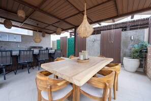 An outdoor dining area with a wooden table and chairs, hanging wicker lamps, and a grill station. - Above The Arch: Penthouse w/ Private Rooftop Pool (Cabo San Lucas)