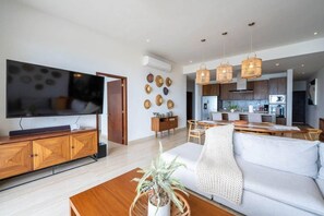 A modern living room with a flat-screen TV, wooden furniture, a dining area, and a kitchen in the background. - Above The Arch: Penthouse w/ Private Rooftop Pool (Cabo San Lucas)