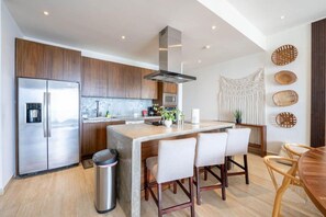 A modern kitchen with a stainless steel refrigerator, a central island with bar stools, and a dining table with chairs. - Above The Arch: Penthouse w/ Private Rooftop Pool (Cabo San Lucas)