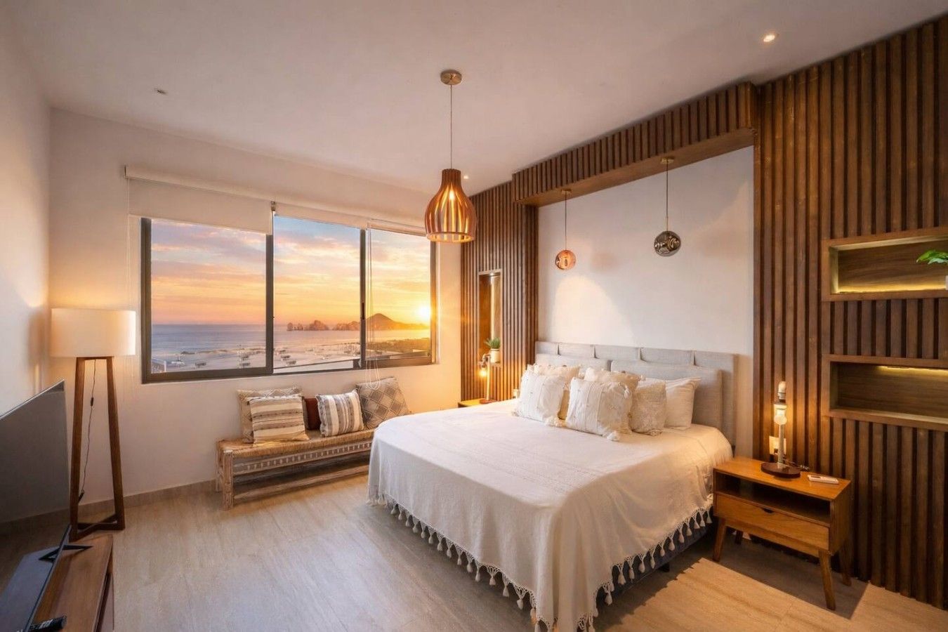 Ein modernes Schlafzimmer mit einem großen Bett, Blick auf den Sonnenuntergang, einem Holzkopfstück und einem Nachttisch mit Lampe.