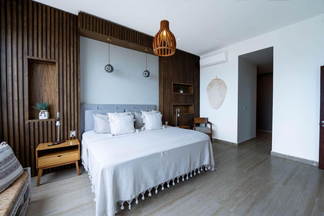 A modern bedroom with a large bed, wooden panel walls, a hanging light fixture, and a small side table.
