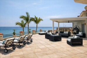 A terrace with outdoor seating, palm trees, and a view of the sea. - The Beachhouse At Rancho Leonero (Los Cabos)
