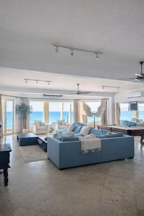 A spacious living room with a large blue sofa, a coffee table, and a view of the sea through large windows. - The Beachhouse At Rancho Leonero (Los Cabos)