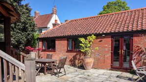 A brick house with a tiled roof, a wooden deck, a potted plant, and a dining table with chairs. - Winston Lodge (Beccles)