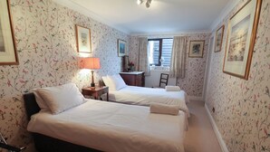 A hotel room with two beds, a desk, a chair, and a window with curtains. - Winston Lodge (Beccles)