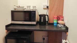 A compact kitchenette with a microwave, kettle, and stacked food containers. - The Gun Room (Beccles)