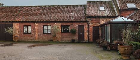 A brick building with a tiled roof, a covered porch, and a gravel driveway.