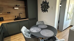 Ett modernt kök med mörka skåp, en bänkskiva i trä och ett runt matbord med tre stolar.