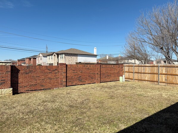 A fenced backyard with a brick wall, a wooden fence, and a grassy area.