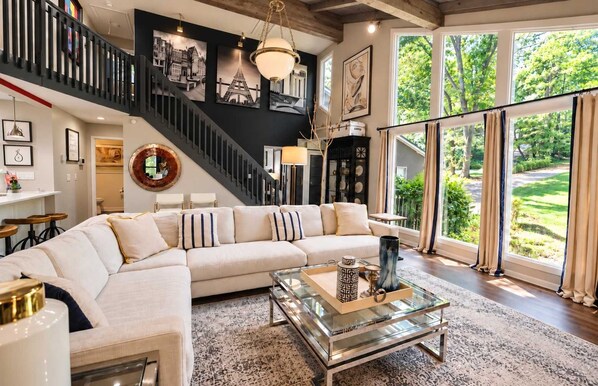 A spacious living room with a large sectional sofa, a glass coffee table, and a staircase leading to an upper level.
