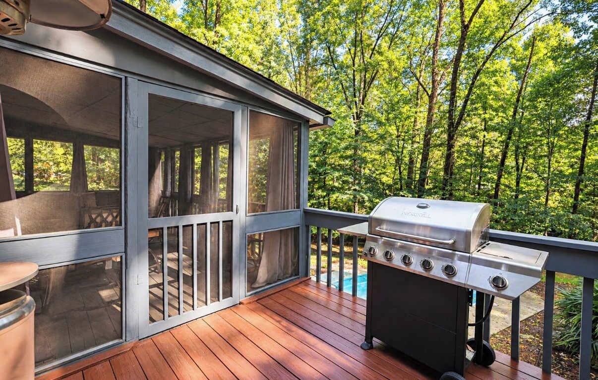 A covered deck with a grill and a pool in the background.