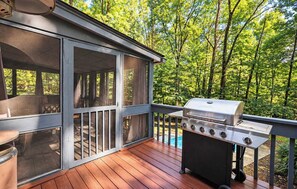 A covered deck with a grill and a pool in the background.