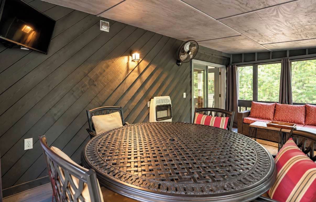 Una habitación con una mesa redonda de metal, sillas, un sofá, un ventilador y una ventana con cortinas.