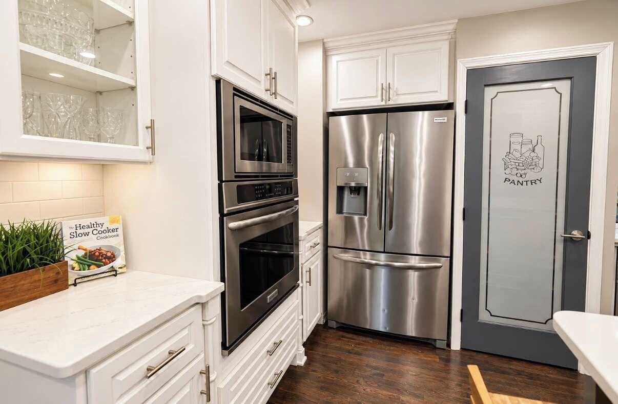 Una cocina con armarios blancos, un refrigerador de acero inoxidable, un microondas y un horno doble.