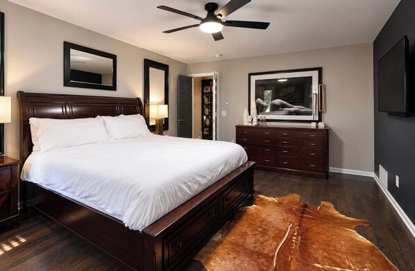 A bedroom with a large bed, a ceiling fan, a dresser, a mirror, and a television.