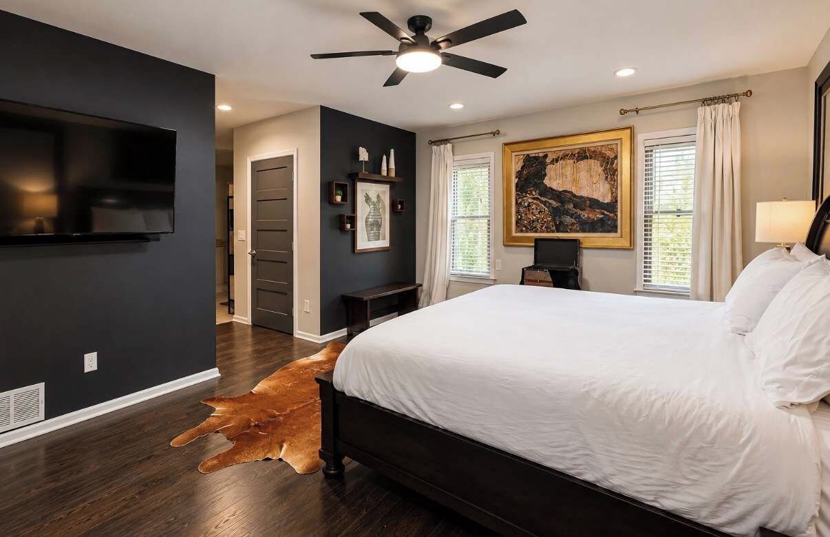 A bedroom with a large bed, a ceiling fan, a mounted TV, and artwork on the walls.