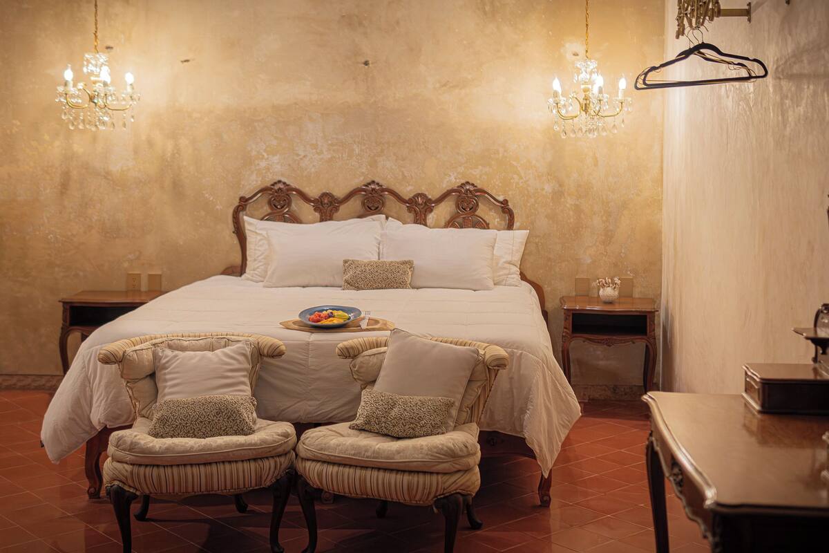 Ein Schlafzimmer mit einem großen Bett, zwei Stühlen, einem Nachttisch und einer Hängeleuchte.