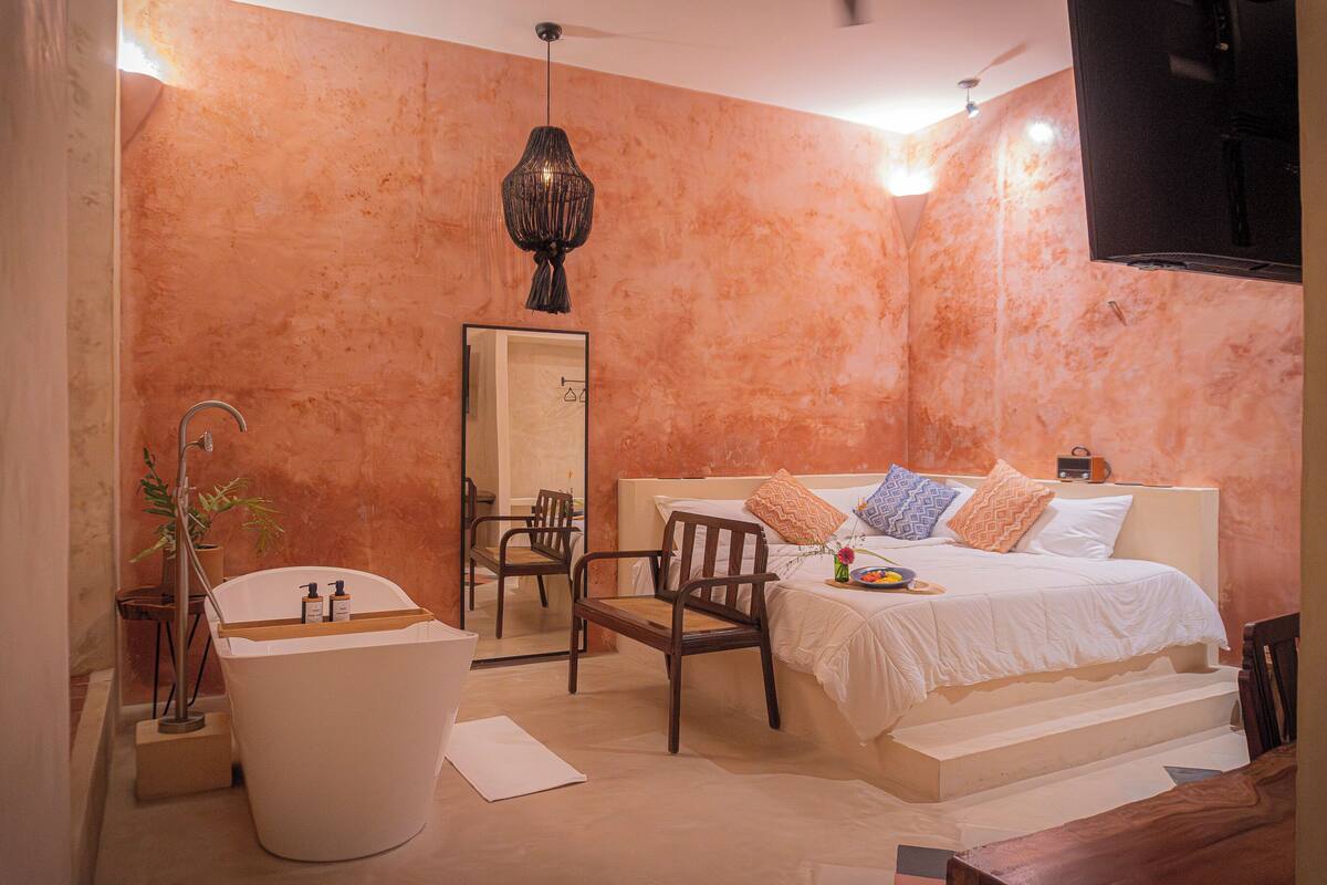 Ein modernes Badezimmer mit Badewanne, Spiegel, Holzstuhl und einem Bett mit Kissen.