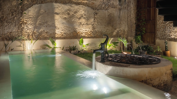 A pool with a water feature, surrounded by plants and a stone wall. - Cien Sueños -Experiential Hotel Boutique (Mérida)
