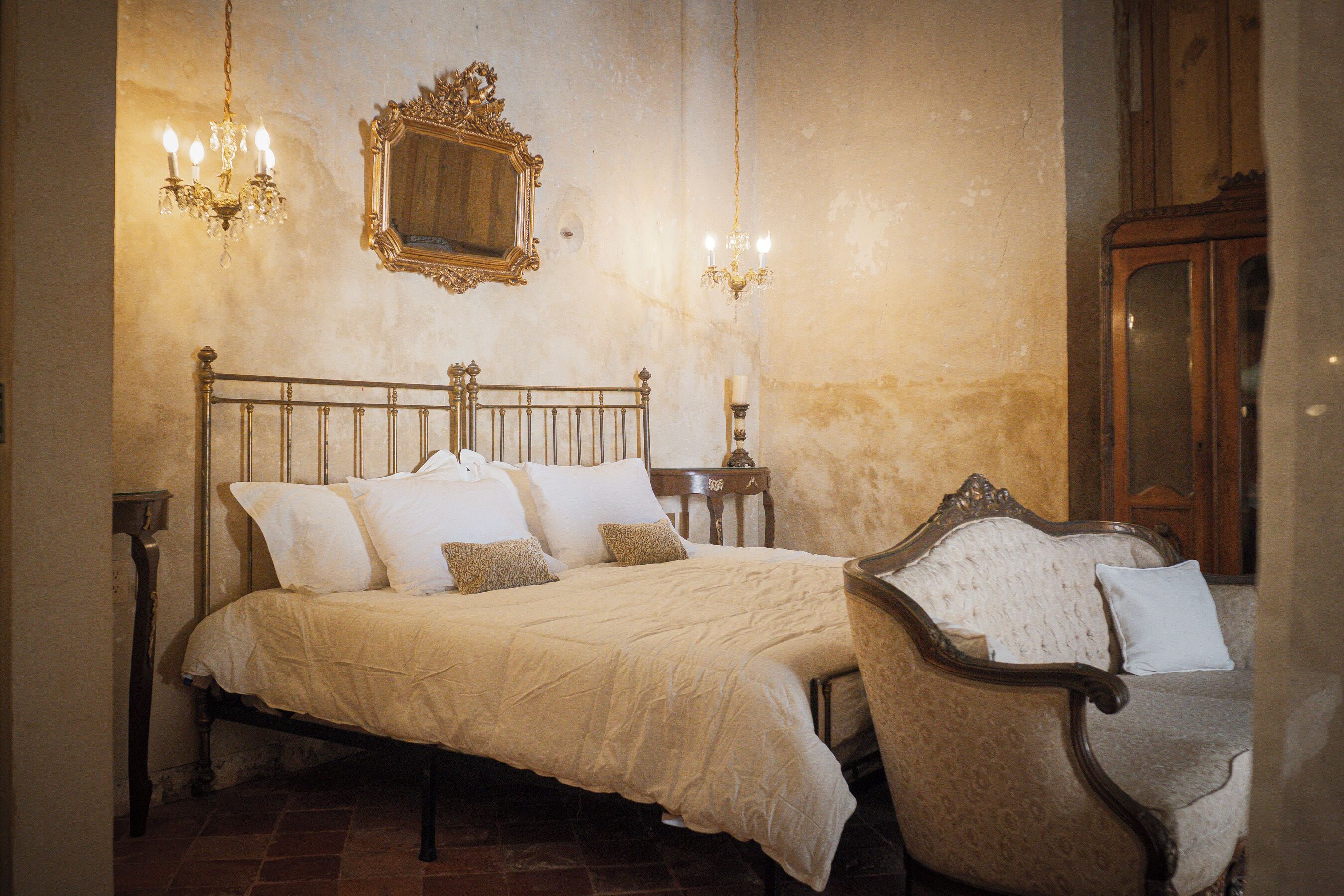 A bedroom with a four-poster bed, a wooden chair, a mirror, and two wall sconces.